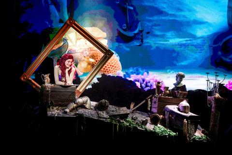 A mermaid in a picture frame among a collection of undersea treasures against digital backdrop of the ocean floor