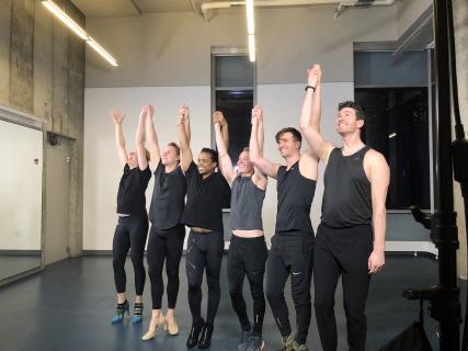 A row of six male dancers raising their hands