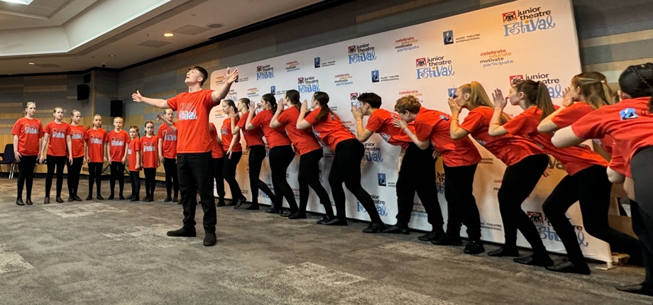 Young people in red JTF tshirts performing, whispering down a line