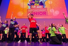 Young people on the stage in front of a sign that says 'We Are Broadway Junior' in different poses